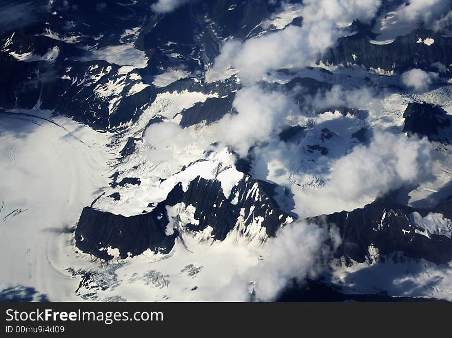 Black mountains viewed from above covered with white glacier with clouds floating above it. Black mountains viewed from above covered with white glacier with clouds floating above it.