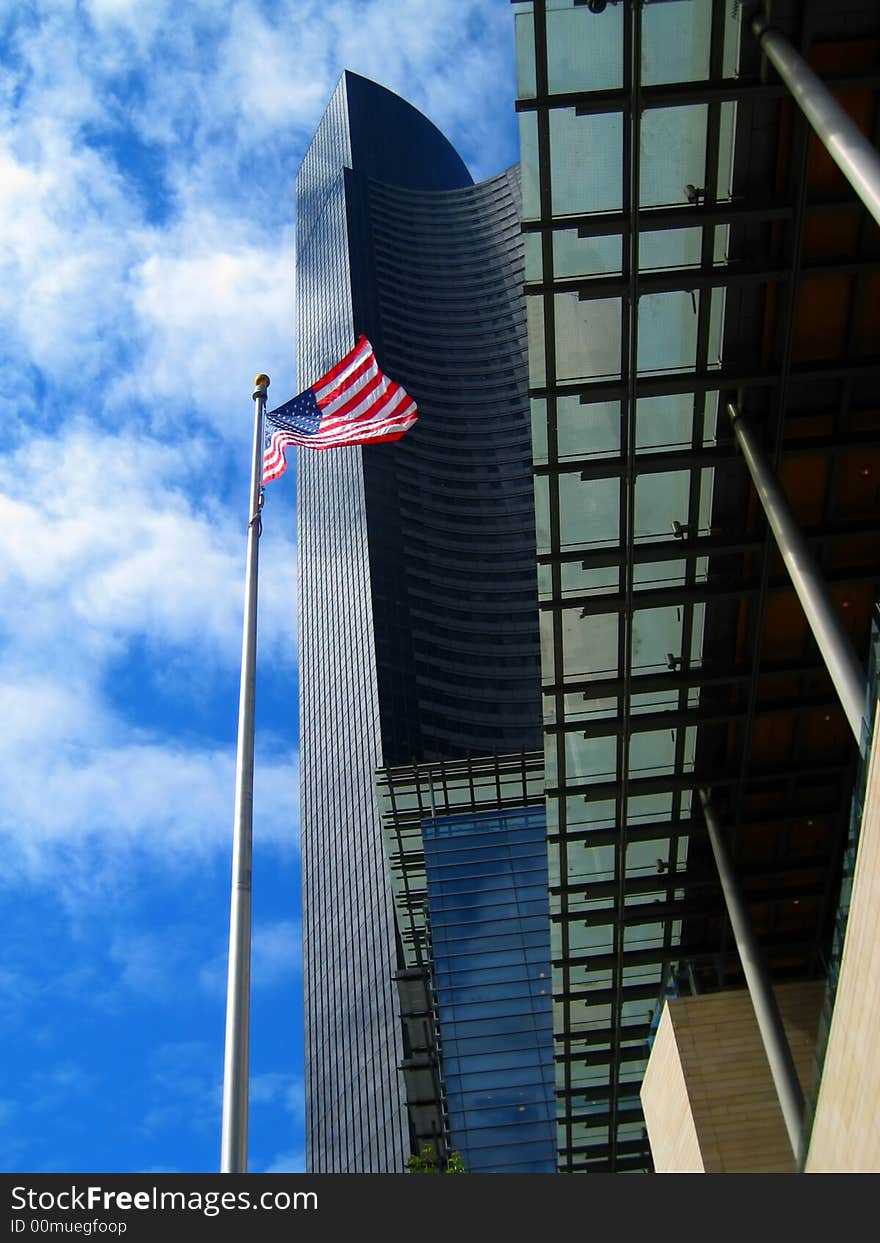 The Red White and Blue of the Flad of the United States of America is waving proudly from this perfect ground level beneath the looming skyscraper that is part of downtown Seattle's skyline. The Red White and Blue of the Flad of the United States of America is waving proudly from this perfect ground level beneath the looming skyscraper that is part of downtown Seattle's skyline