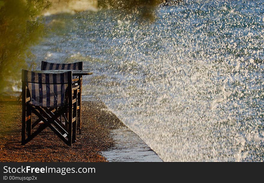 Image shows an empty table and chairs on a berth hit by rough sea waves. Image shows an empty table and chairs on a berth hit by rough sea waves