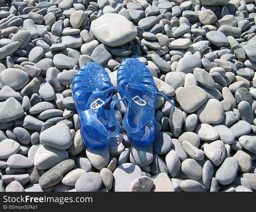 Blue plastic sandals on a pebble beach. Blue plastic sandals on a pebble beach