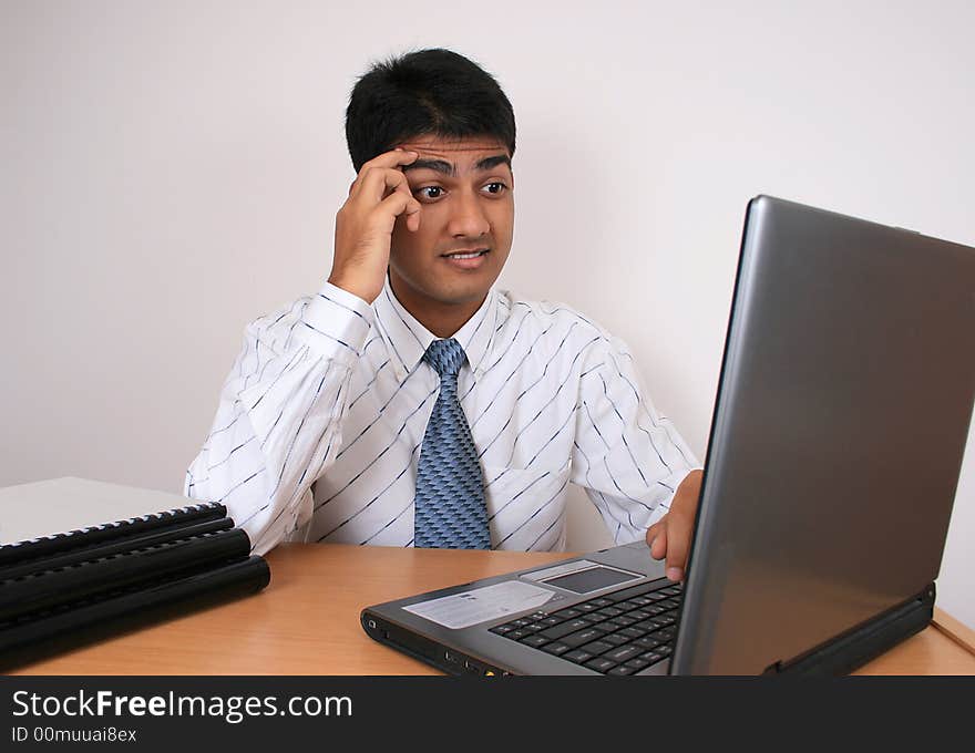 Young Indian business man working at his desk. Has a puzzled look.(Series). Young Indian business man working at his desk. Has a puzzled look.(Series)