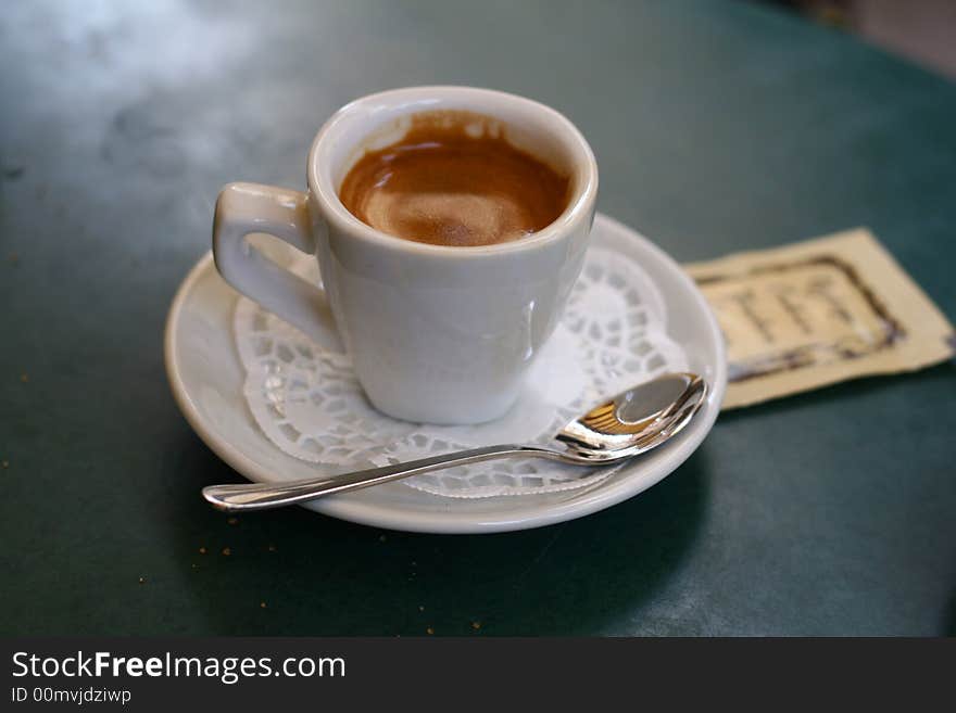 White cup of coffee with a ferrous spoon on a green table