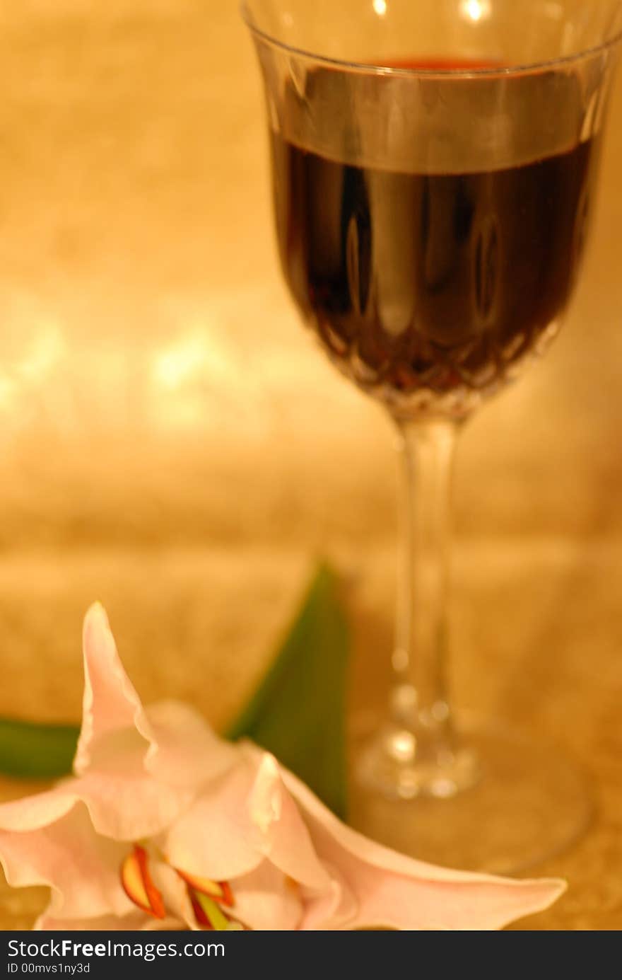 Glass of red wine on golden background and a white lilly next to it. Glass of red wine on golden background and a white lilly next to it