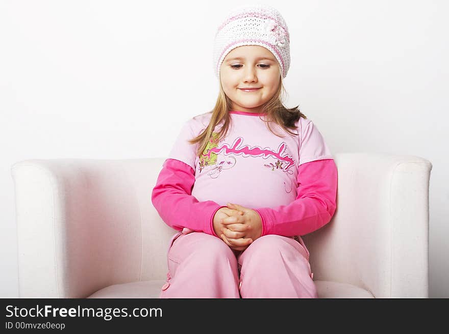 Nice young girl in pink on light background sitting on white chair with teddy bear