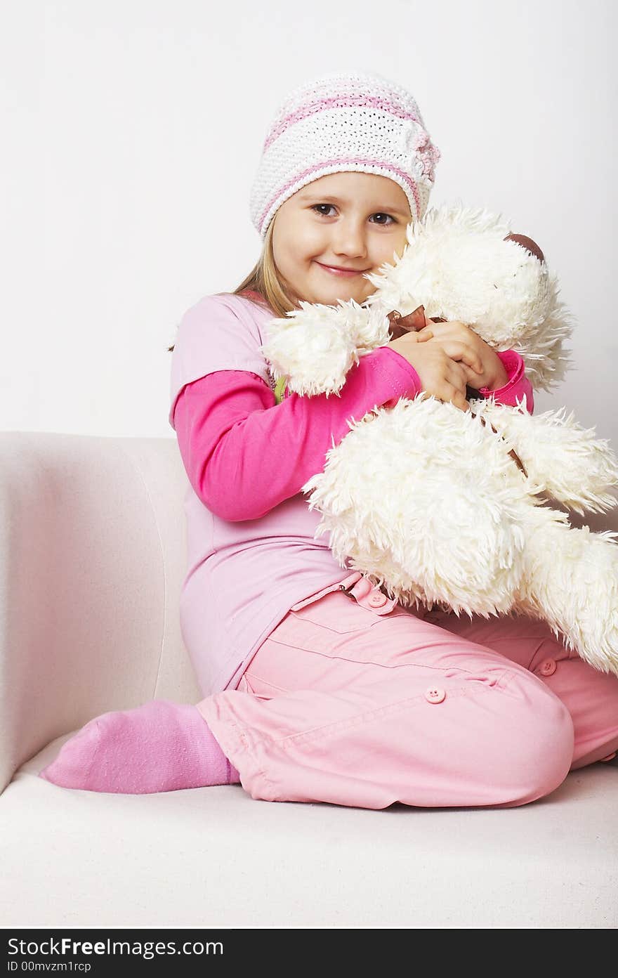 Nice young girl in pink on light background sitting on white chair with teddy bear