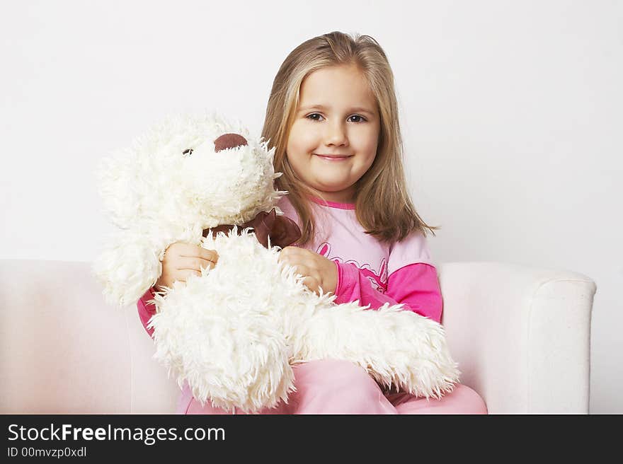 Nice young girl in pink on light background sitting on white chair with teddy bear