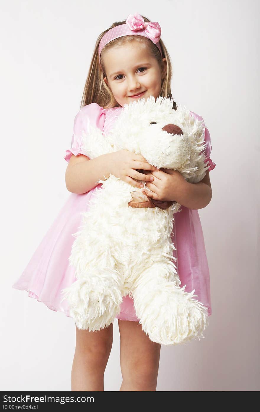 Nice young girl in pink on light background standing on white chair with teddy bear