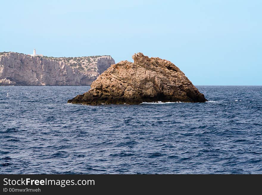 Large rock in the water near the west coast of Ibiza, Conejera island with its lighthouse Cabo Blanco in the background. Large rock in the water near the west coast of Ibiza, Conejera island with its lighthouse Cabo Blanco in the background