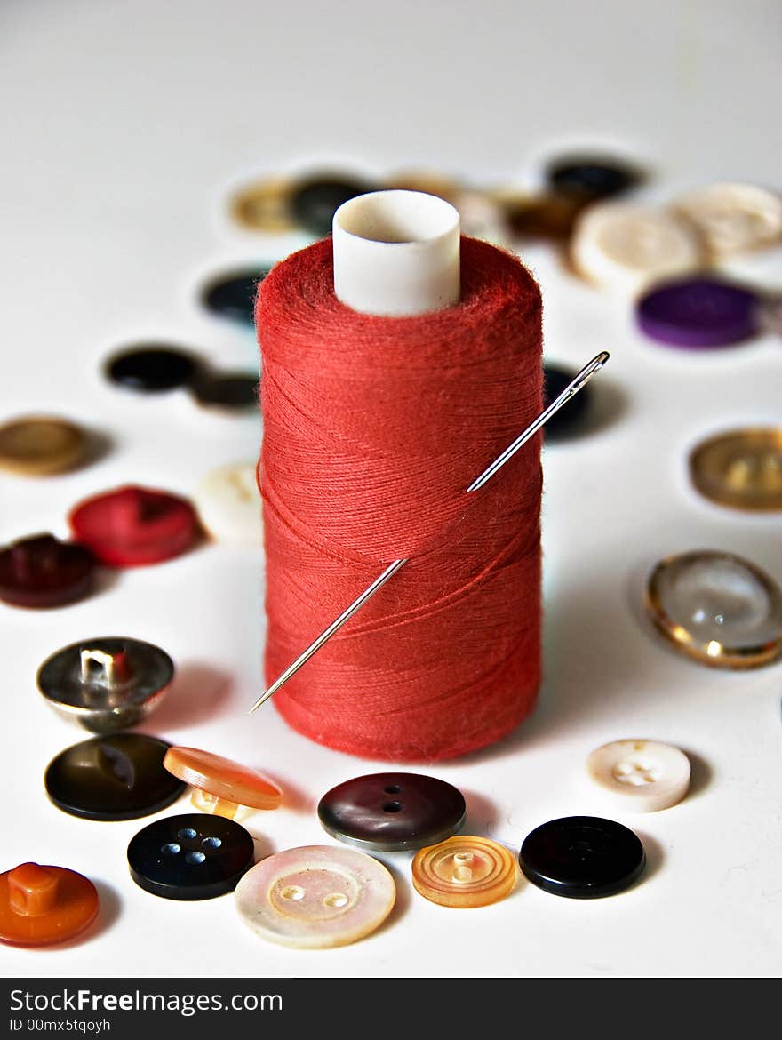 Reel of red thread with needle and scattered buttons. Reel of red thread with needle and scattered buttons