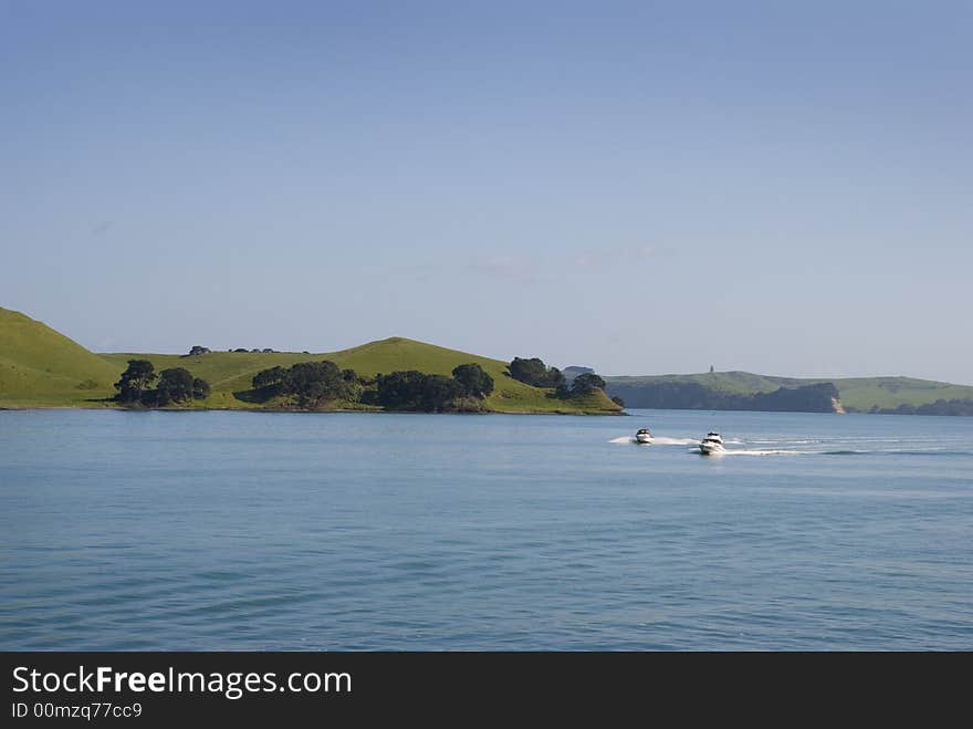 Two boats race past an island leaving a wake behind them. Two boats race past an island leaving a wake behind them