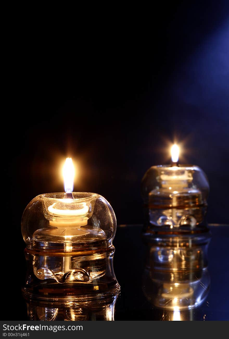 2 burning candles on glass table with dark and blue background