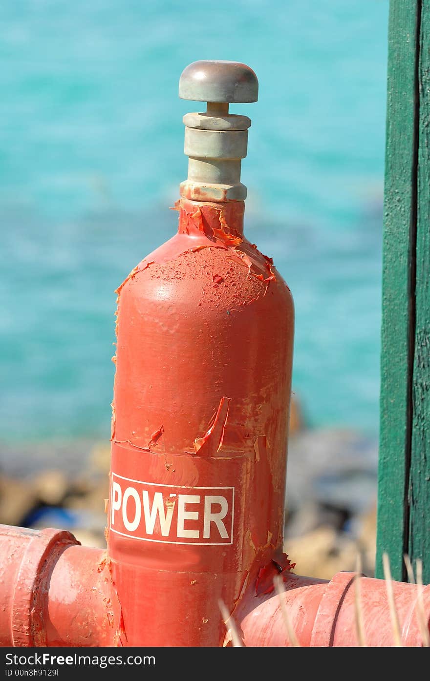 A close up view of a red gas cylinder attached to an above ground pipeline with water from the Red Sea in the background. A close up view of a red gas cylinder attached to an above ground pipeline with water from the Red Sea in the background.