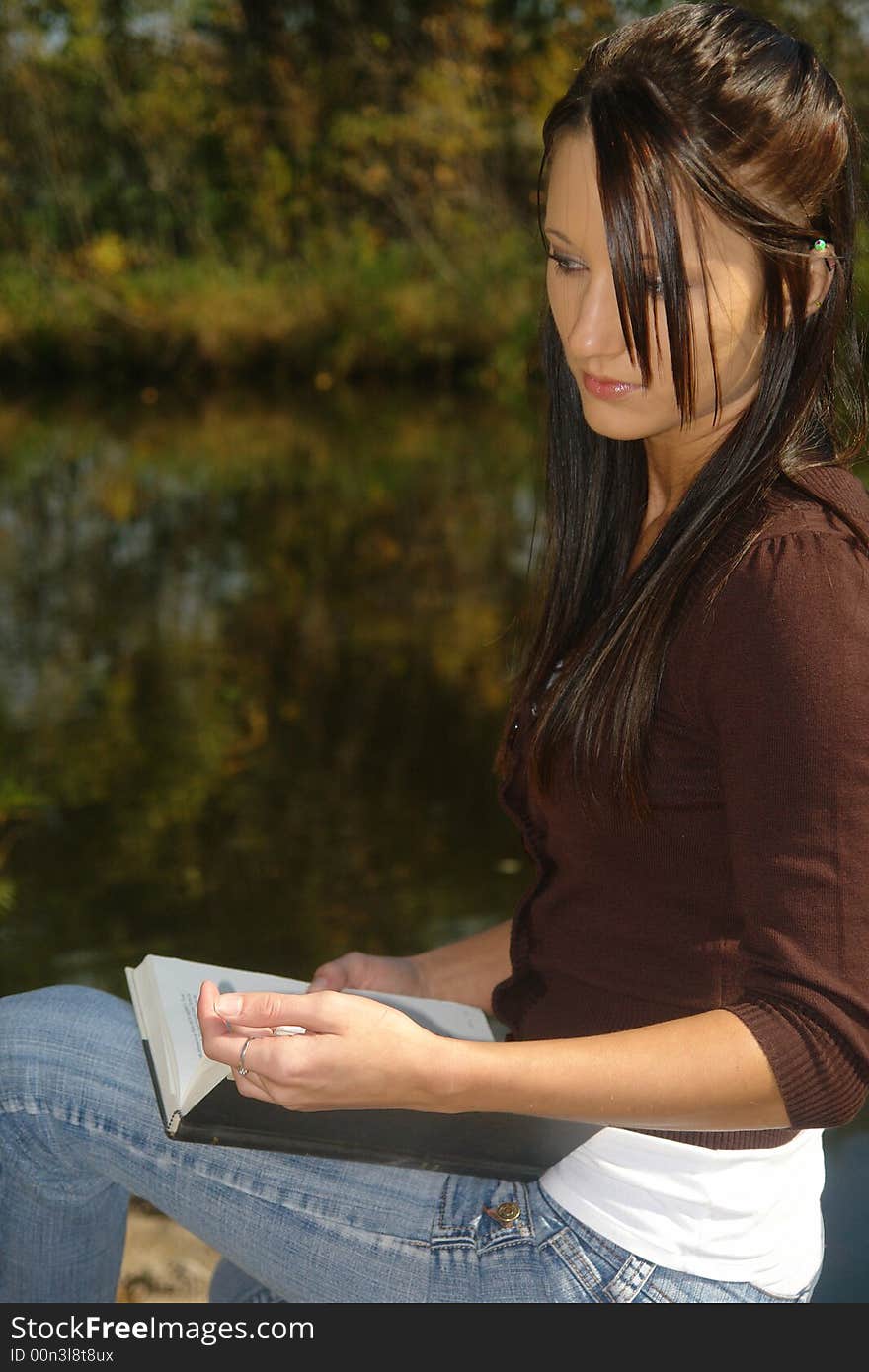 A picture of a beautiful woman reading and comtemplating by water. A picture of a beautiful woman reading and comtemplating by water