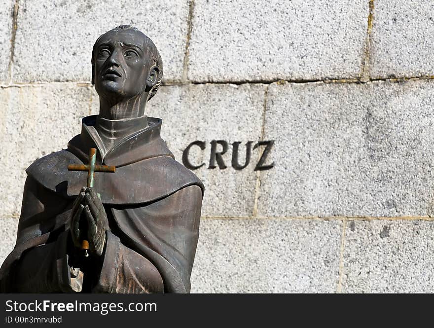 A statue of a friar praying with a cross in his hands and the word cross in Spanish. A statue of a friar praying with a cross in his hands and the word cross in Spanish