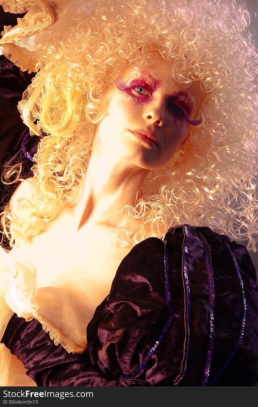 Girl like a doll with curly blond hair and extravagant make-up and in medieval clothes