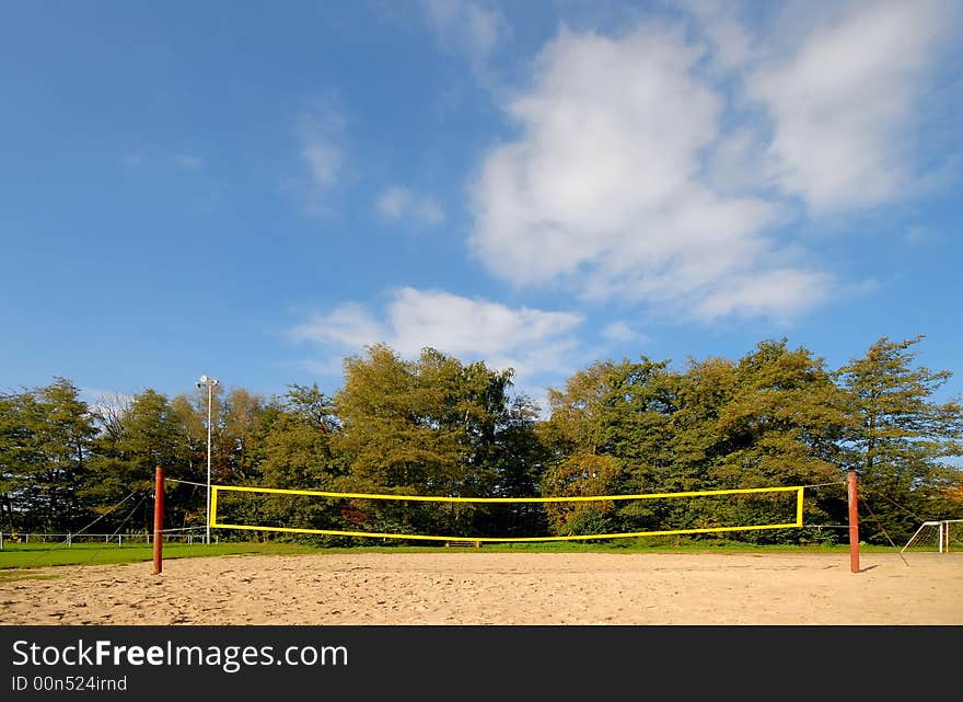 Yellow volleyball net under blue clouded sky, in the background autumn trees