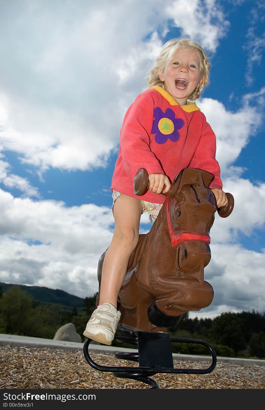 Cute young girl riding a play pony on a sunny day at the park. Cute young girl riding a play pony on a sunny day at the park