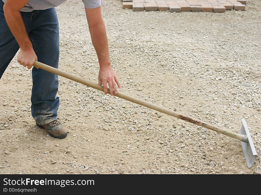 Close up of one male construction worker bending over pushing rake leveling dirt. Close up of one male construction worker bending over pushing rake leveling dirt