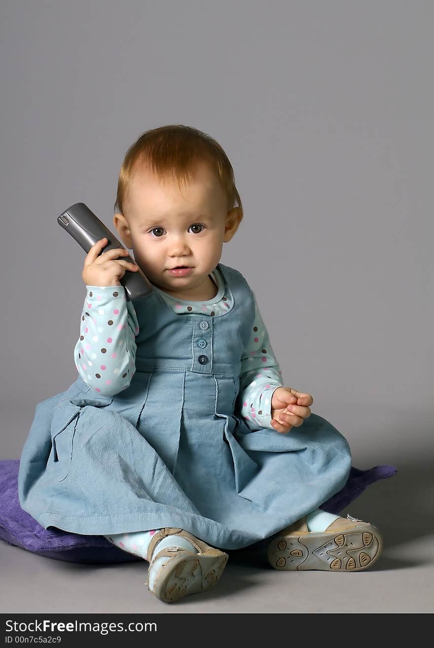 The child calling by phone on a grey background with a smile