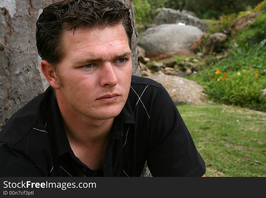 Young Male Model sitting against a tree in the park. Young Male Model sitting against a tree in the park