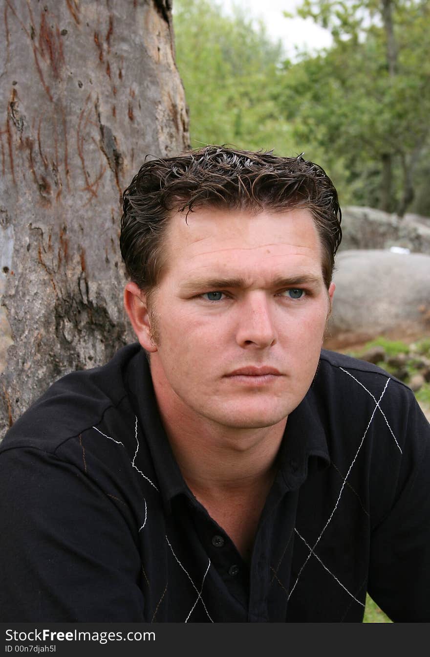 Young Male Model sitting against a tree in the park. Young Male Model sitting against a tree in the park