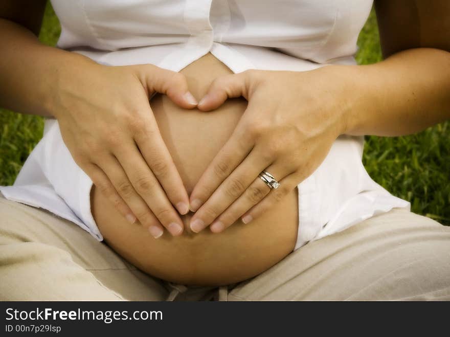 Mother to be makes a heart shape on her tummy with her hands. Mother to be makes a heart shape on her tummy with her hands