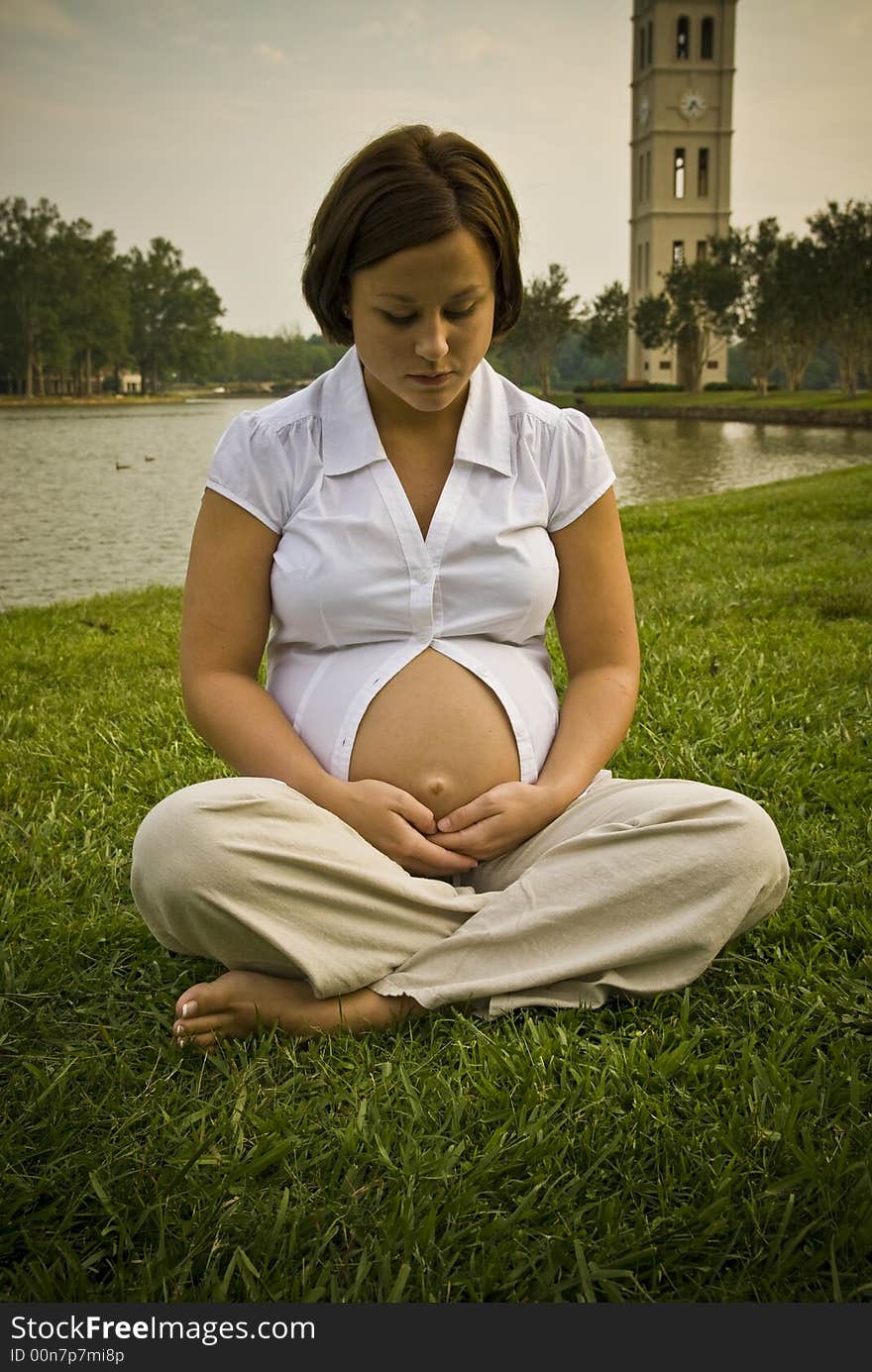 Mom to be sitting on grass looking down at her tummy. Mom to be sitting on grass looking down at her tummy