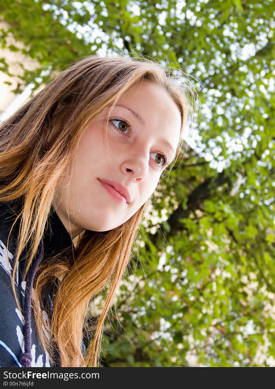 The lovely girl stands under a green tree. The lovely girl stands under a green tree