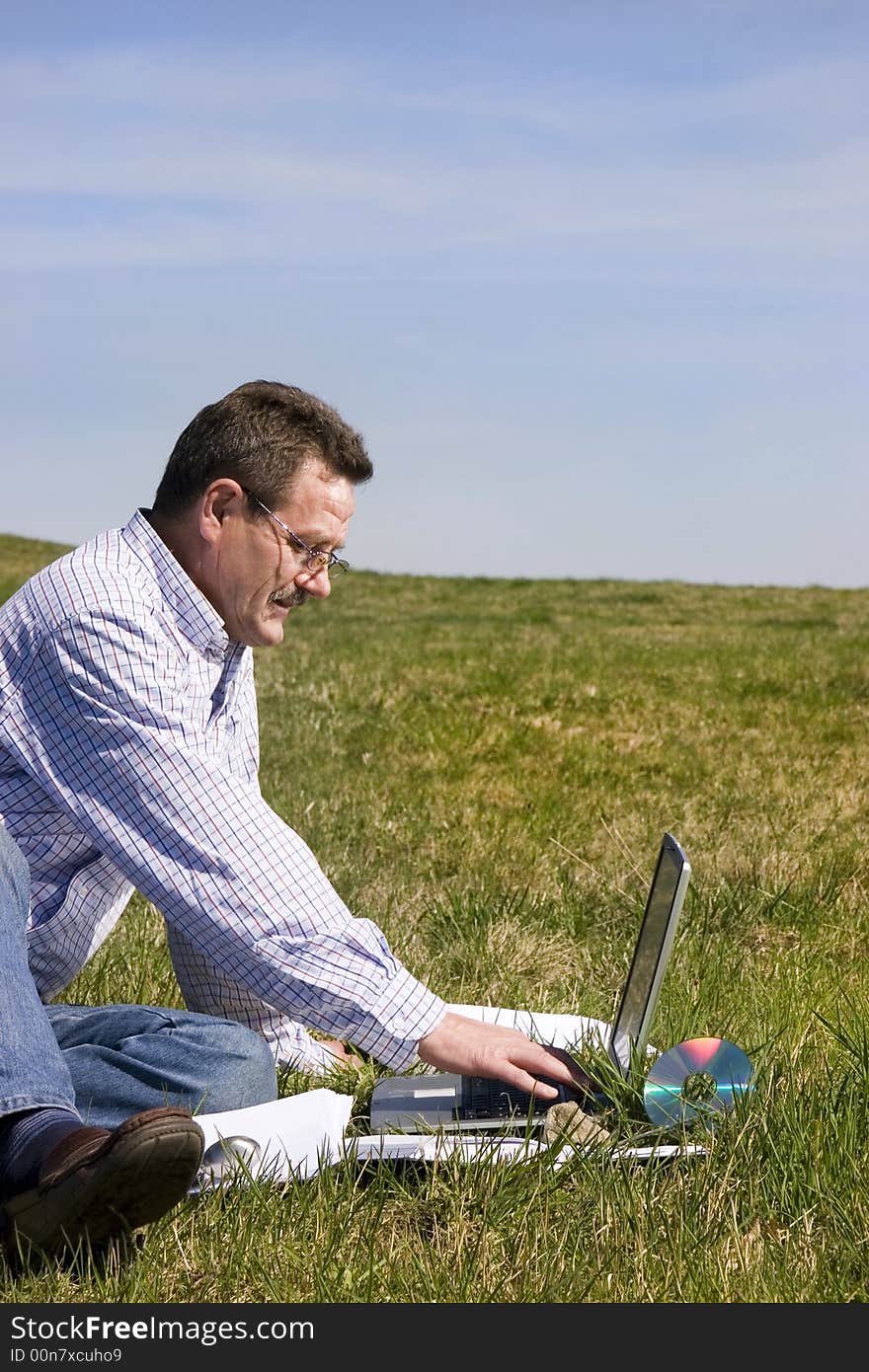 Businessman sittingloo on the grass with his laptop, seen from the profile. Businessman sittingloo on the grass with his laptop, seen from the profile.