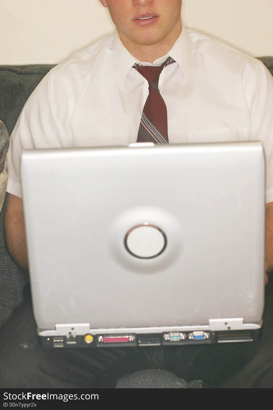 Front close-up view of young man with loose tie holding laptop on knees as he sits on sofa. Front close-up view of young man with loose tie holding laptop on knees as he sits on sofa