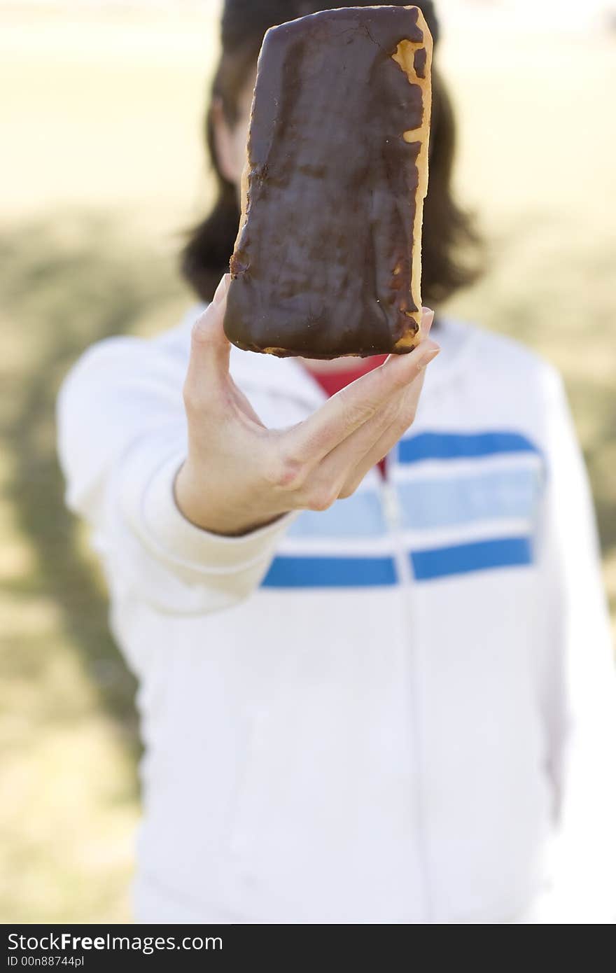 Close-up shot of young woman wearing casual clothing holding, displaying chocolate donut bar, waist-up. Close-up shot of young woman wearing casual clothing holding, displaying chocolate donut bar, waist-up