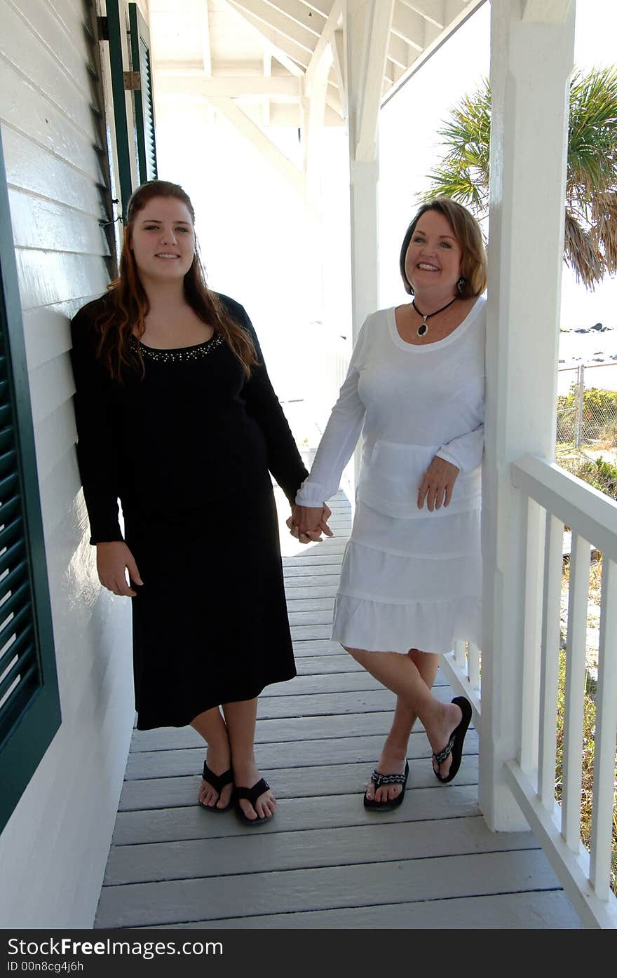 Two women of different generations holding hands standing on the porch of a beach house. Two women of different generations holding hands standing on the porch of a beach house