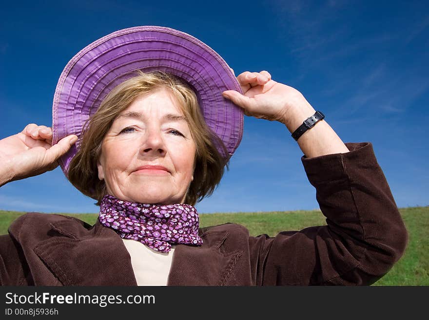 Mature and cheerful, joyful and happy woman enjoying life on a meadow, having fun with her violet hat - presenting good condition and healthy life :). Mature and cheerful, joyful and happy woman enjoying life on a meadow, having fun with her violet hat - presenting good condition and healthy life :)