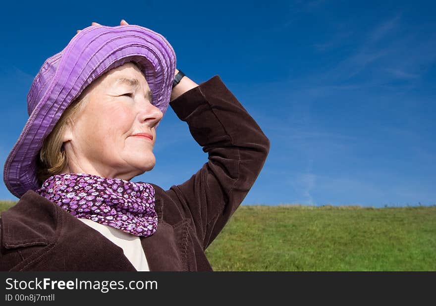 Mature and cheerful, joyful and happy woman enjoying life on a meadow, having fun with her violet hat - presenting good condition and healthy life :). Mature and cheerful, joyful and happy woman enjoying life on a meadow, having fun with her violet hat - presenting good condition and healthy life :)