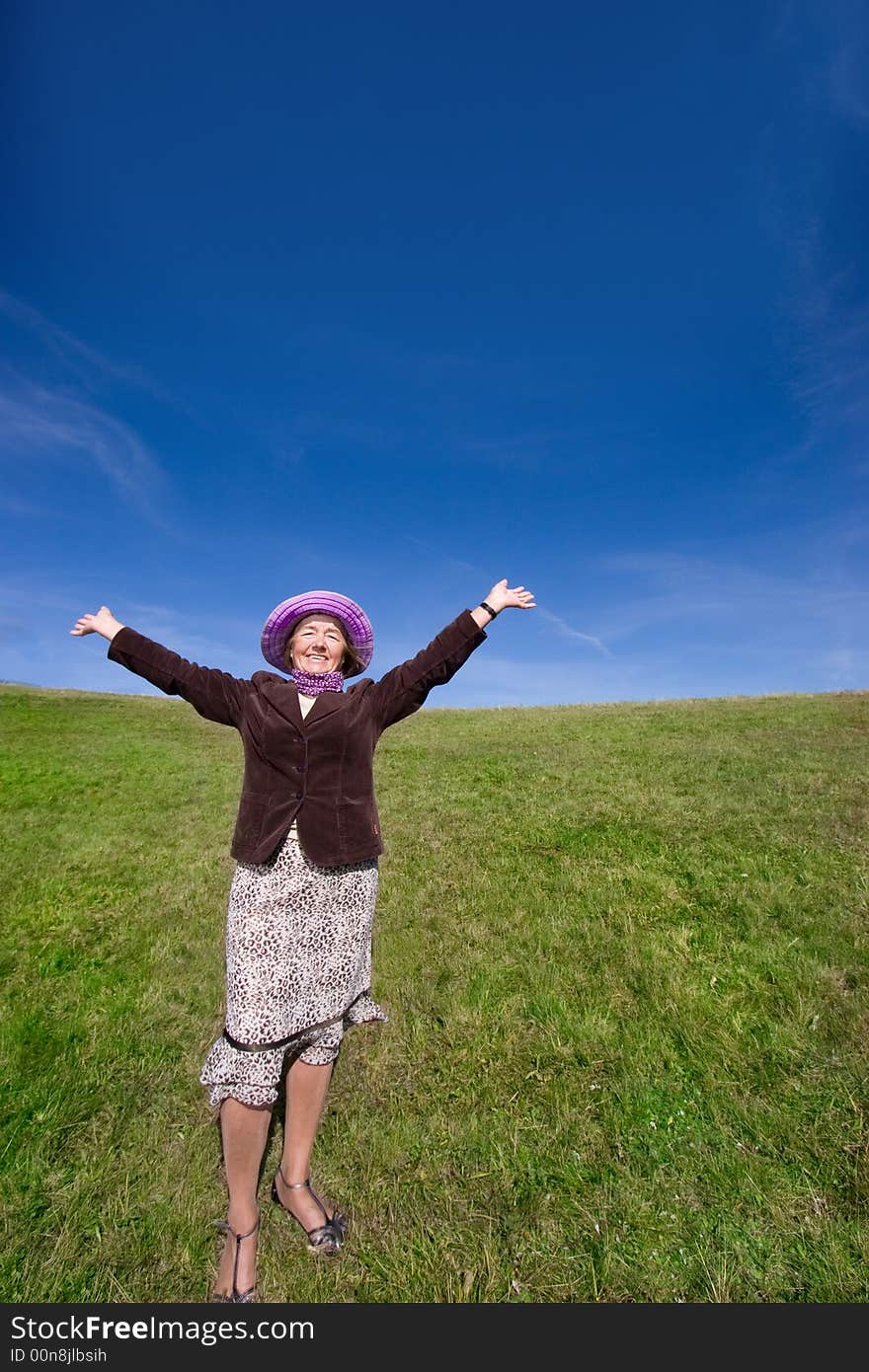 Mature and cheerful, joyful and happy woman enjoying life on a meadow, having fun with her violet hat - presenting good condition and healthy life :). Mature and cheerful, joyful and happy woman enjoying life on a meadow, having fun with her violet hat - presenting good condition and healthy life :)