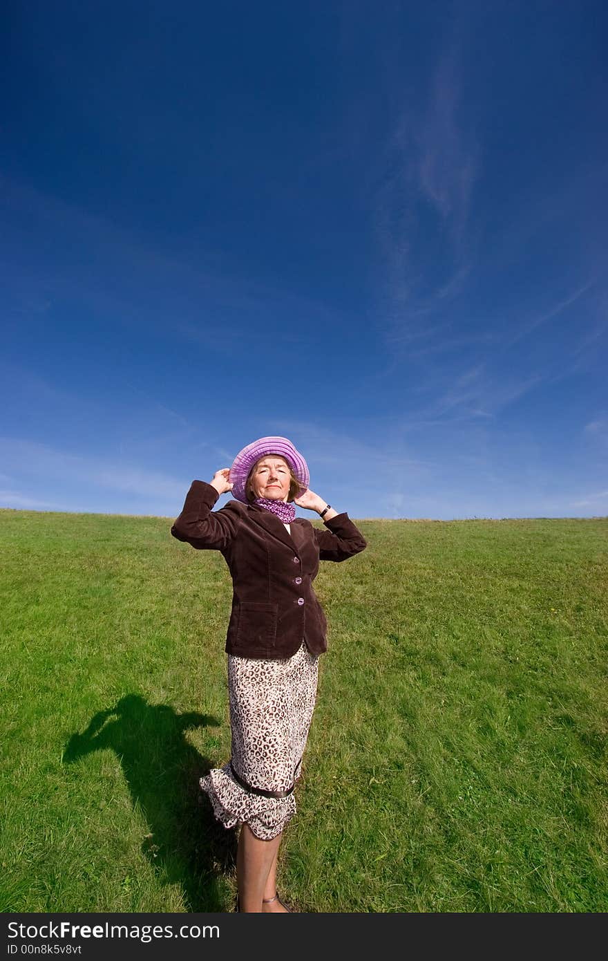 Mature and cheerful, joyful and happy woman enjoying life on a meadow, having fun with her violet hat - presenting good condition and healthy life :). Mature and cheerful, joyful and happy woman enjoying life on a meadow, having fun with her violet hat - presenting good condition and healthy life :)