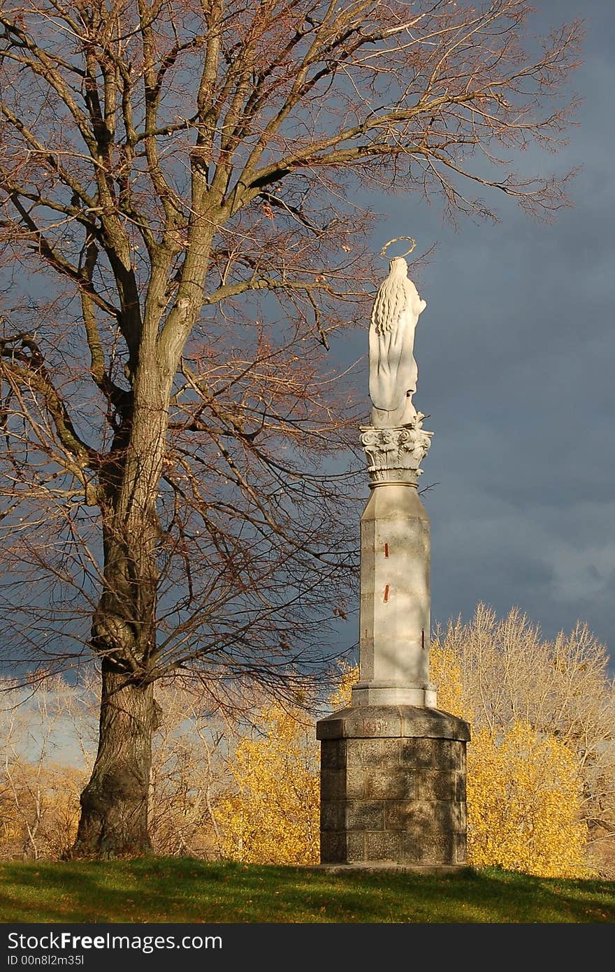 Holy sculpture on high post under the tree with dark blue sky behind. Holy sculpture on high post under the tree with dark blue sky behind