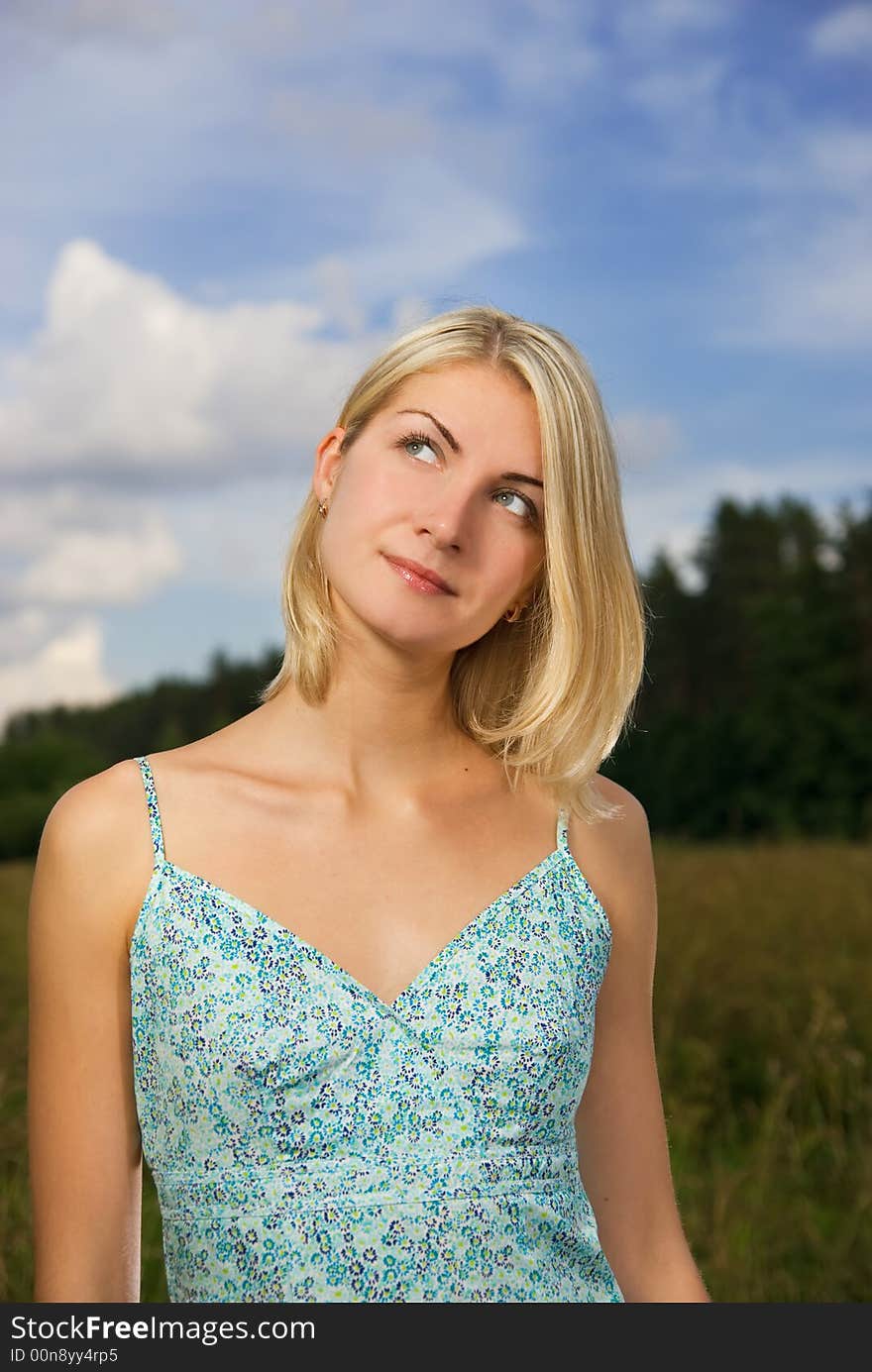 Beautiful blond girl in the field, blue cloudy sky behind her