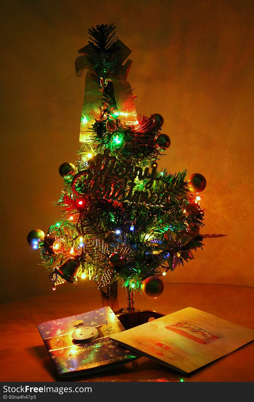 Small, but beautifully lit up and decorated artificIal Christmas tree with greeting cards at base.