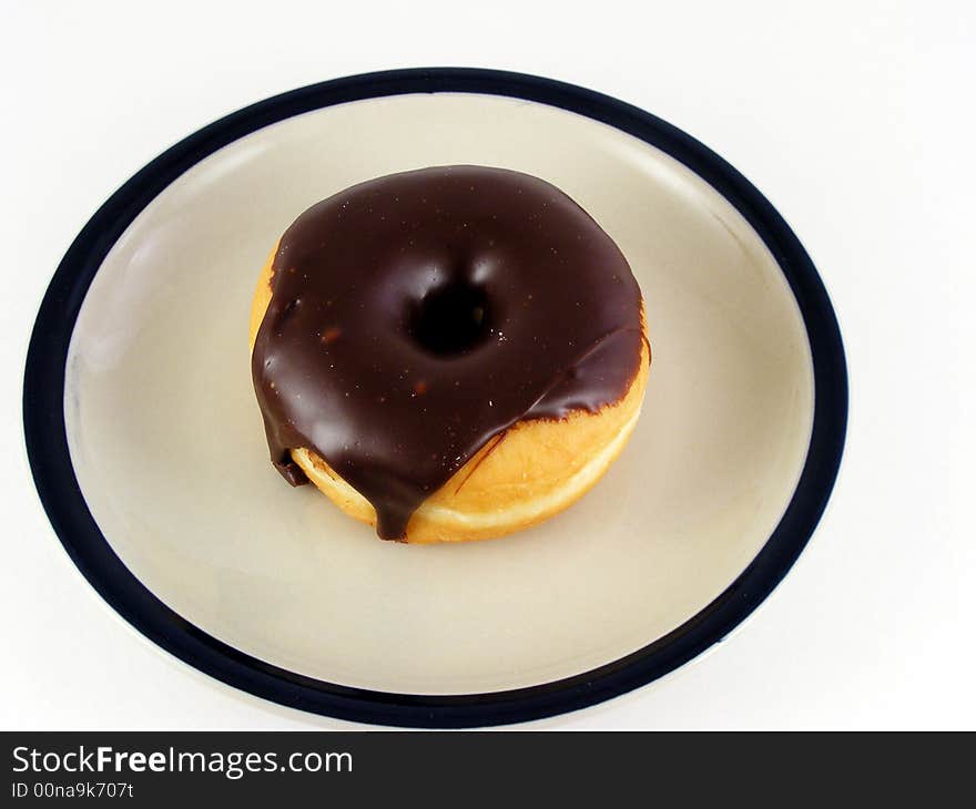 A chocolated iced donut on a plate against a white background. A chocolated iced donut on a plate against a white background.