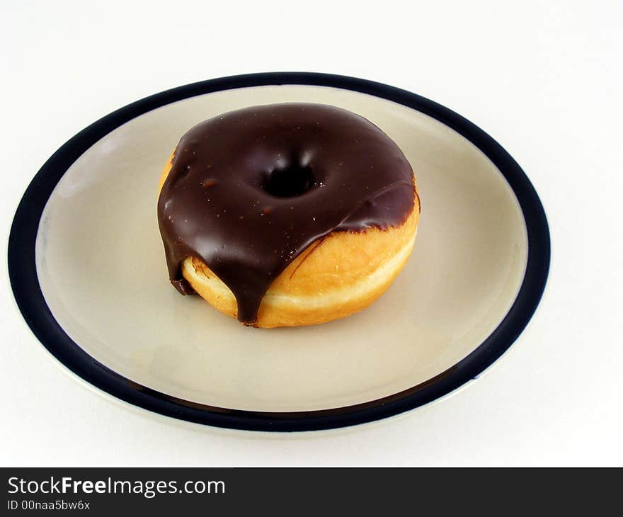 A chocolated iced donut on a plate against a white background. A chocolated iced donut on a plate against a white background.