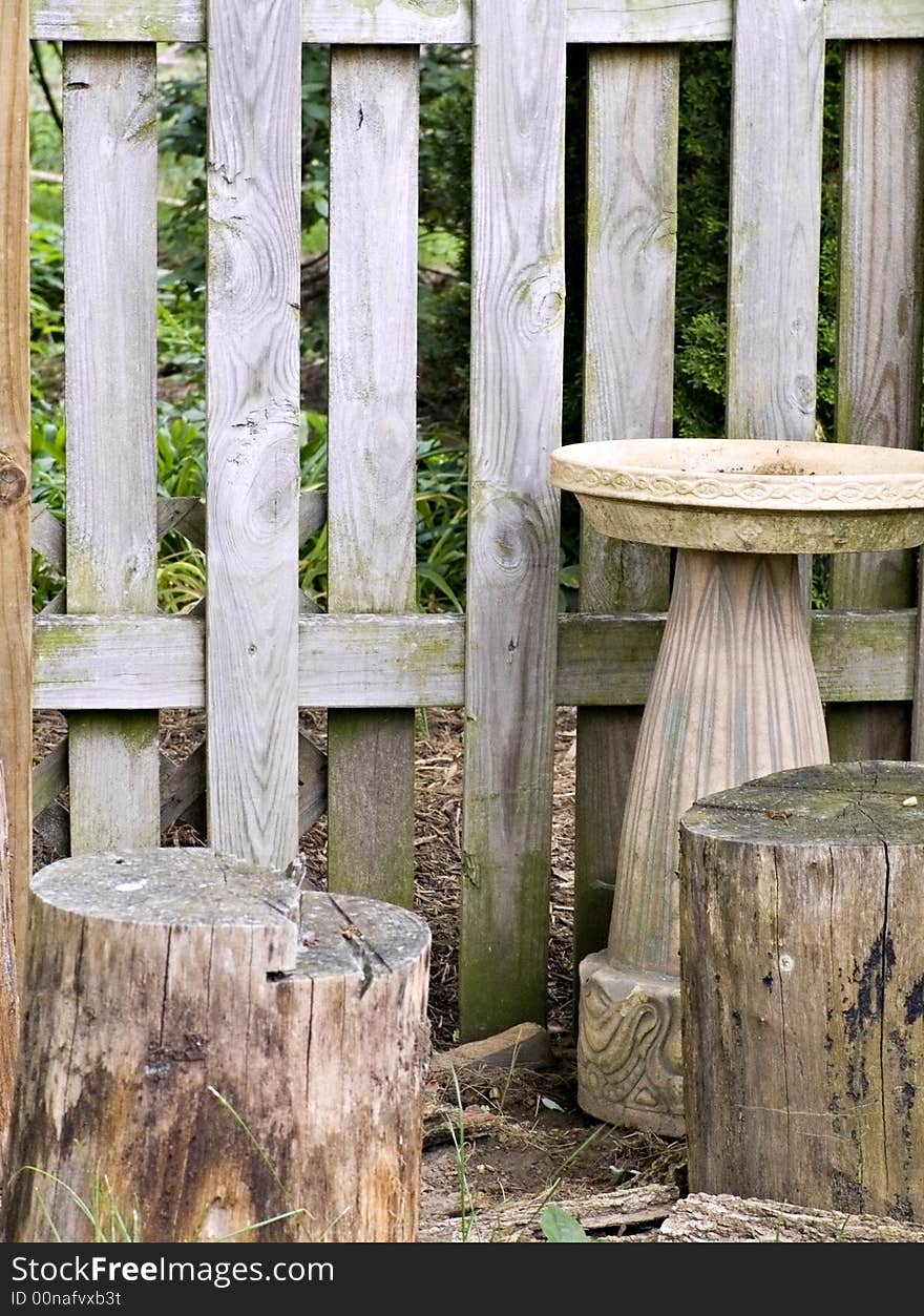 The corner of a garden with ornamental birdbath and stumps.