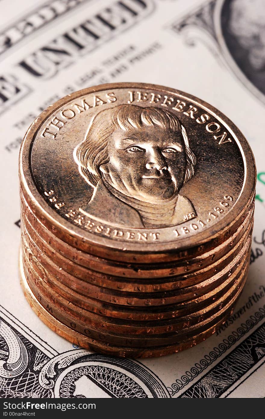 Vertical close-Up of a Jefferson dollar coin on a stack of dollar coins with an out-of-focus paper dollar bill in the background. Vertical close-Up of a Jefferson dollar coin on a stack of dollar coins with an out-of-focus paper dollar bill in the background.