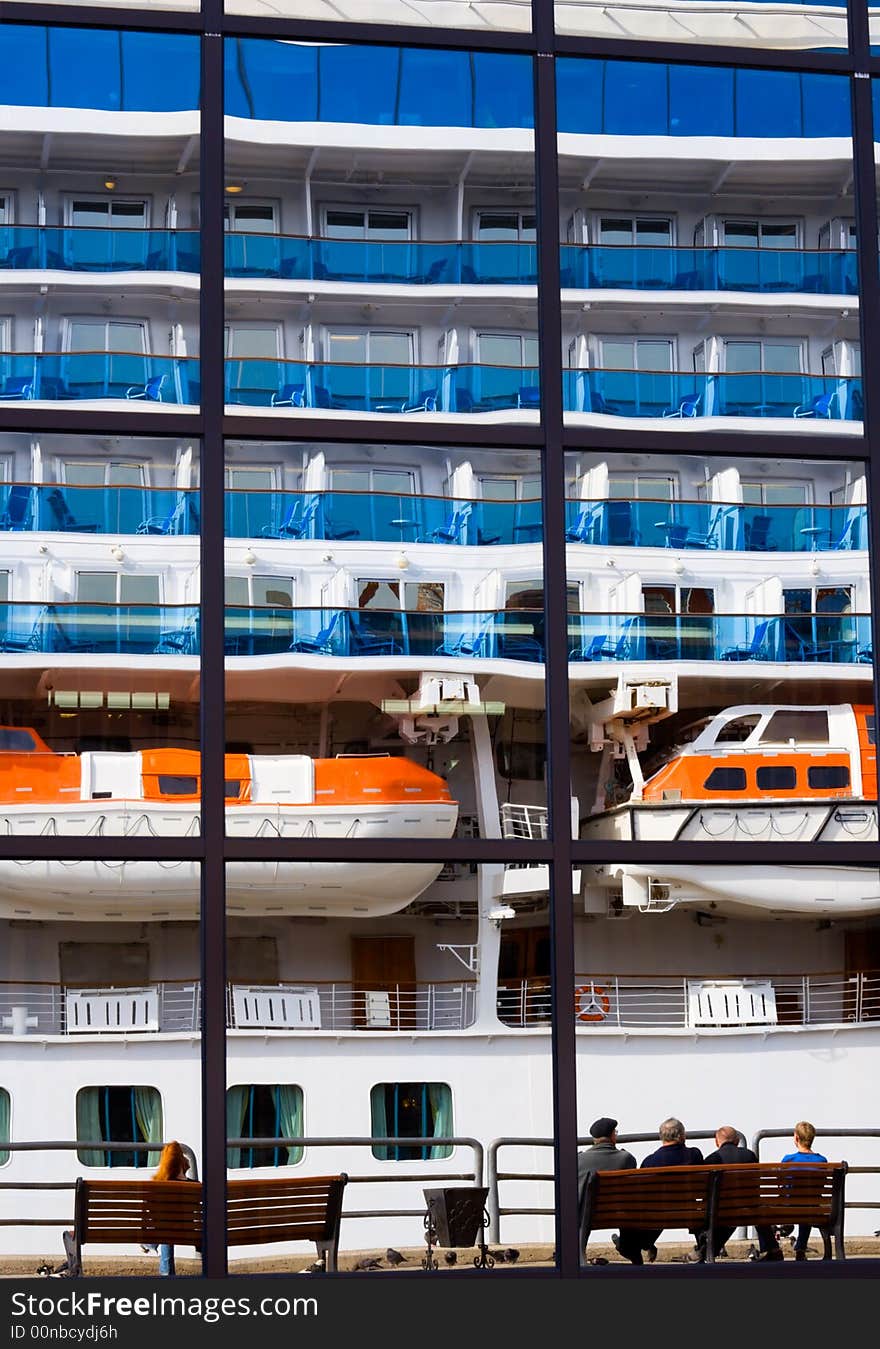 Russia. Round the world cruise ship is leaving from port Vladivostok. Reflection of the liner on the marine passenger terminal. Some people siting here on a benches. Russia. Round the world cruise ship is leaving from port Vladivostok. Reflection of the liner on the marine passenger terminal. Some people siting here on a benches.