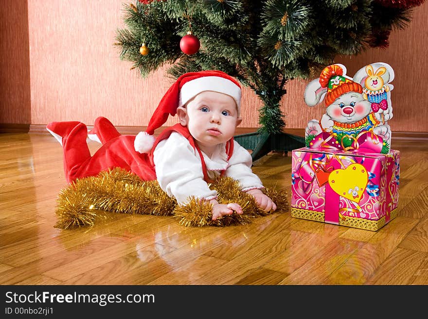 Little baby as Santa in red cap laying on the floor with gifts. Little baby as Santa in red cap laying on the floor with gifts