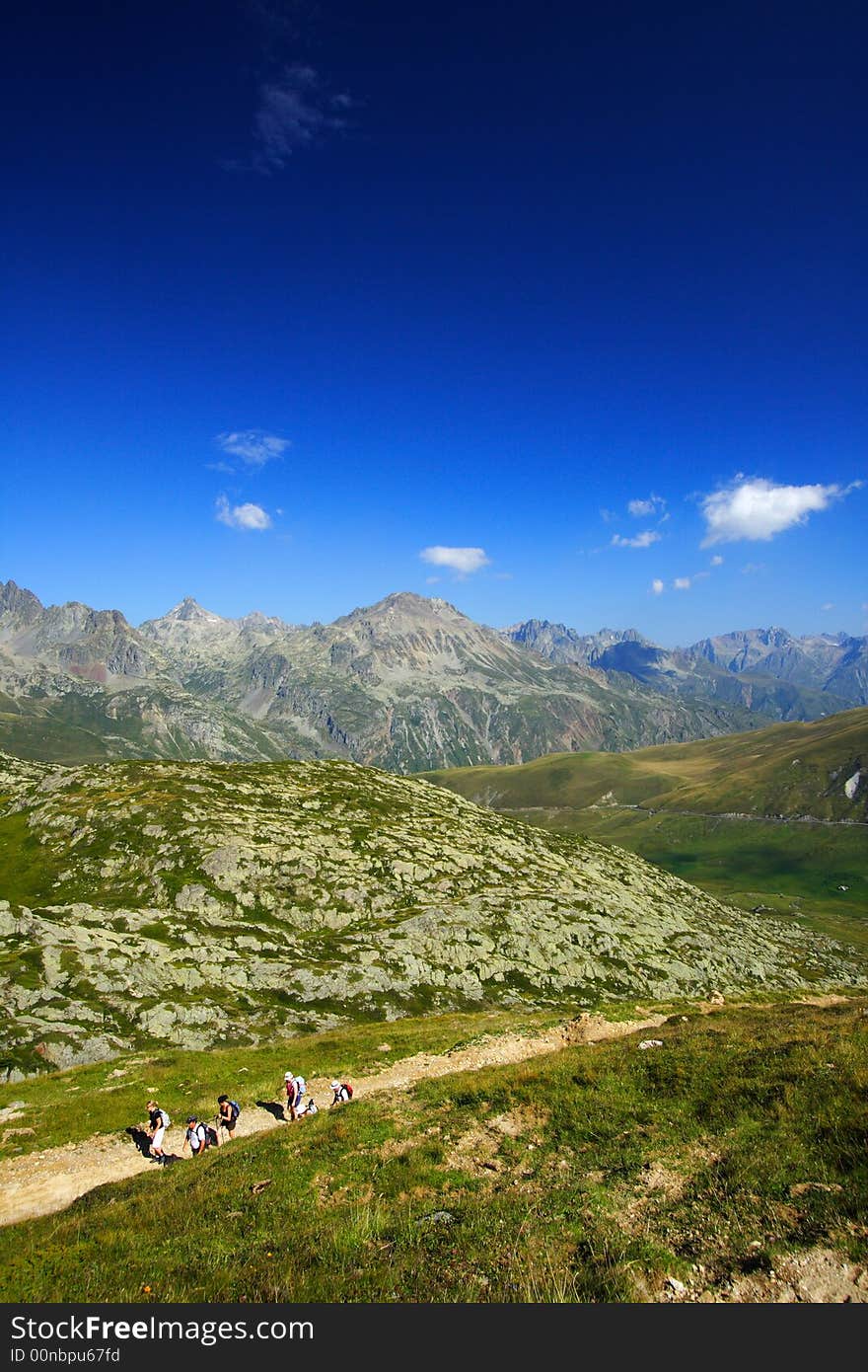 Trekkers walking on the trail by a summer afternoon with a superb panorama on mountains.