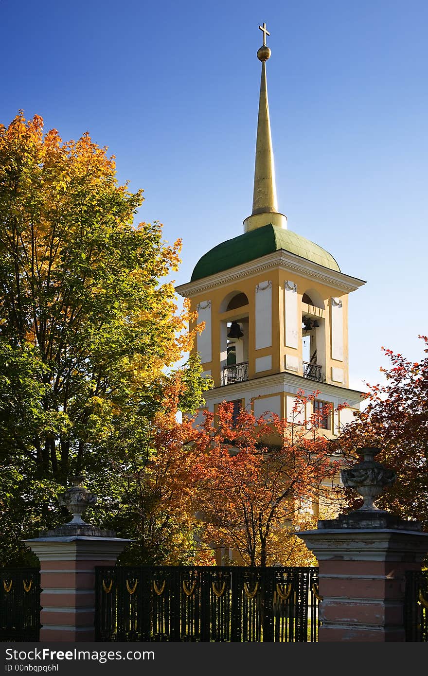 Autumn belltower on a background of the blue sky, surrounded by multi-coloured autumn trees. Autumn belltower on a background of the blue sky, surrounded by multi-coloured autumn trees