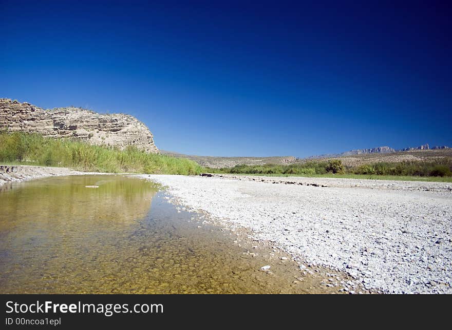 A distant cliff reflecting in the shallow waters of a riverbed. A distant cliff reflecting in the shallow waters of a riverbed.