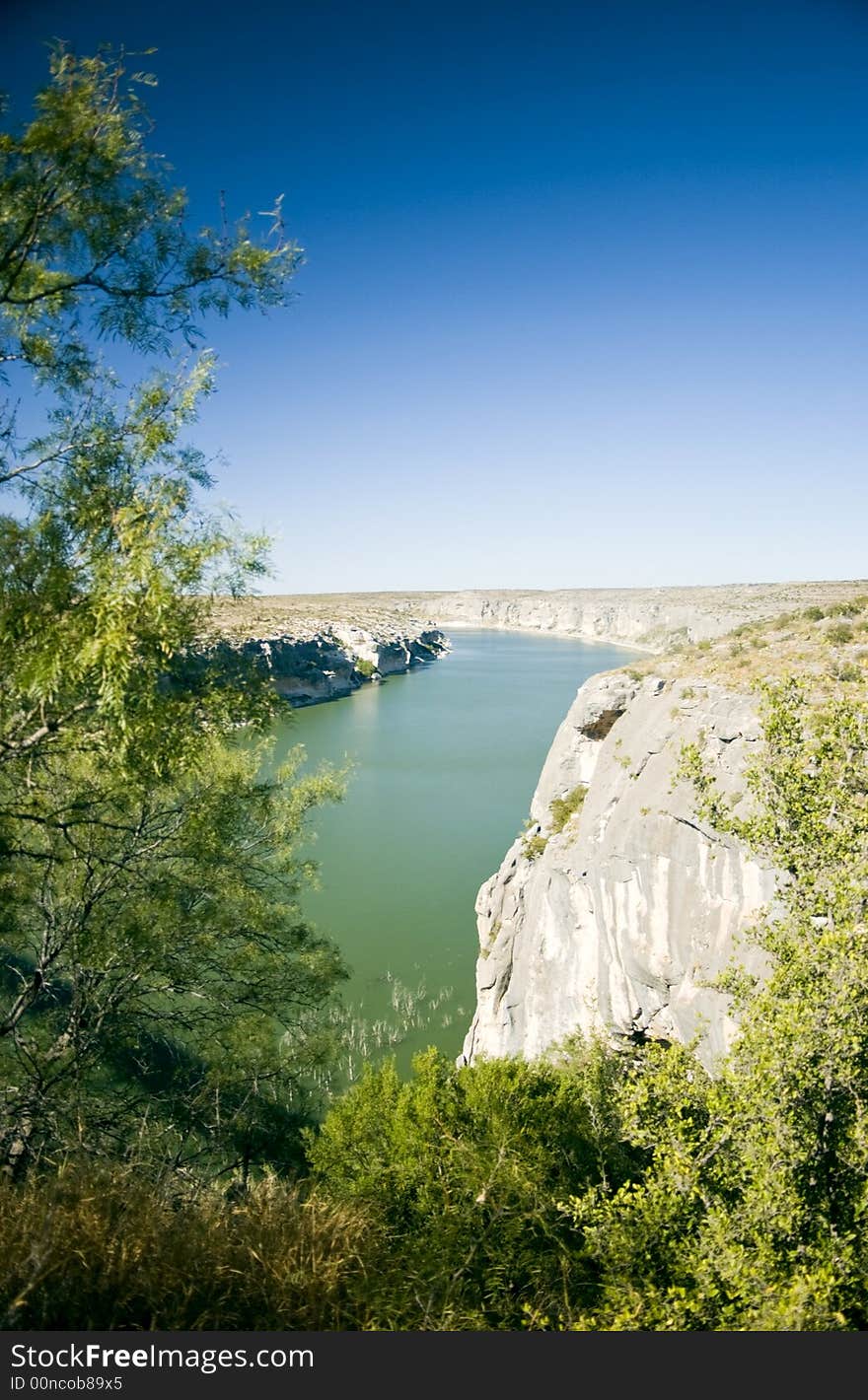 A wide green river bodered by rocky cliffs and enveloped in a bright blue cloudless sky. A wide green river bodered by rocky cliffs and enveloped in a bright blue cloudless sky.