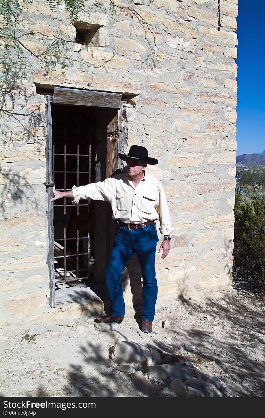 A man in western attire standing outside an old ruin of a jail. A man in western attire standing outside an old ruin of a jail